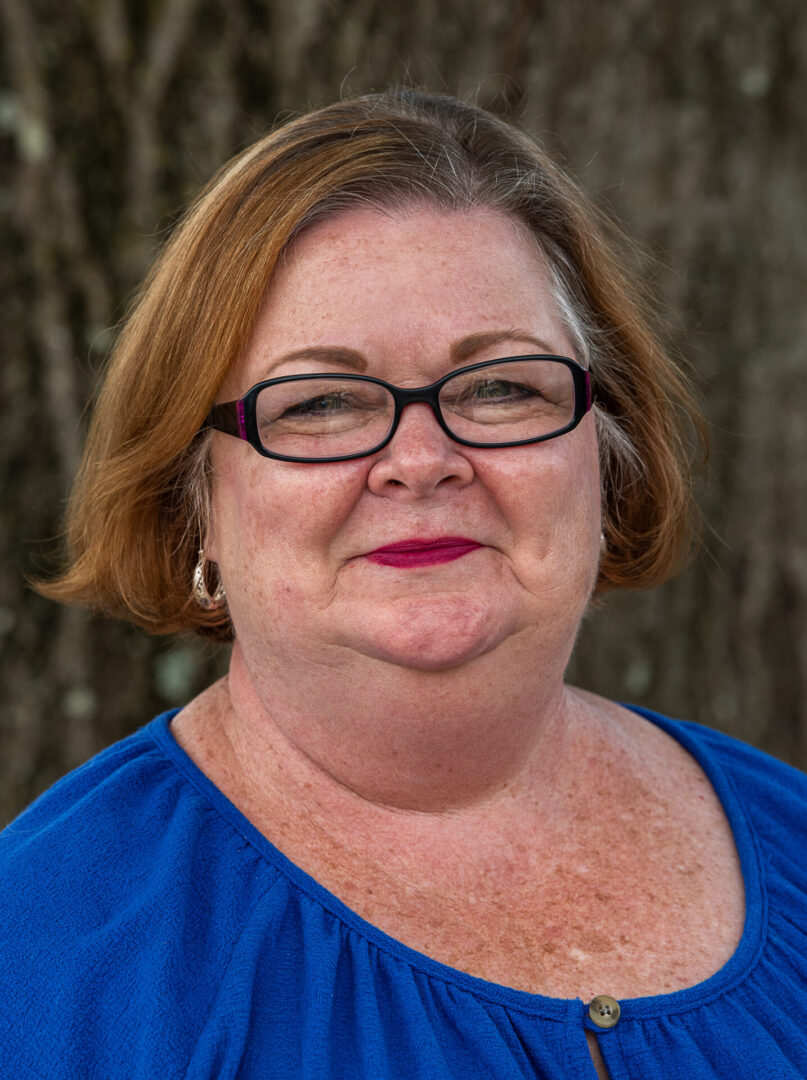 A woman with glasses and red hair wearing blue.