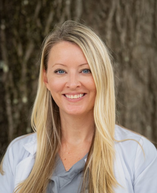 A woman with long blonde hair wearing white lab coat.