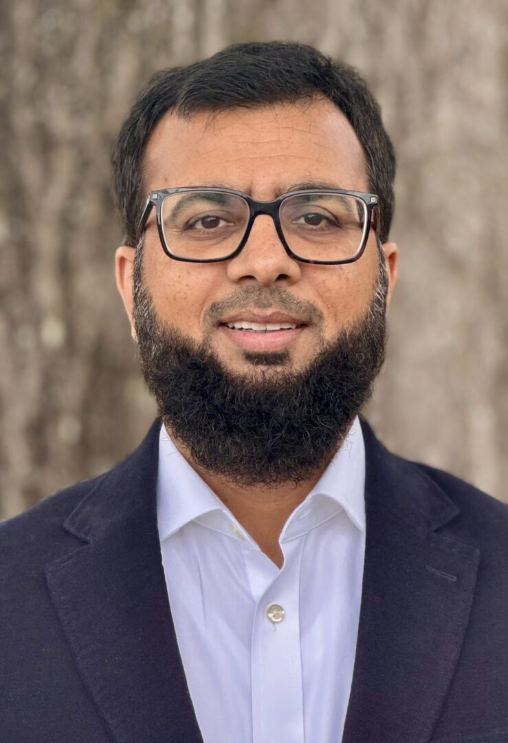 image001 A man with glasses and beard wearing a suit.